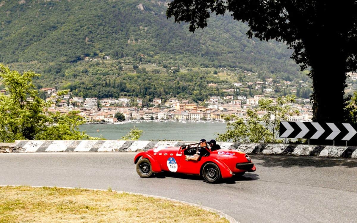 A red car during the 1000 Mille driving past a picturesque scene.