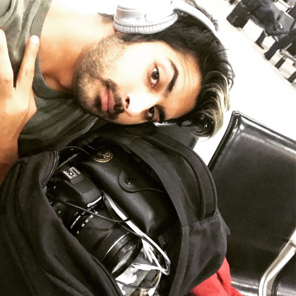 YouTuber Siraj Raval poses with headphones on and a camera in his backpack.