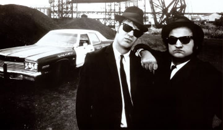 The Blues Brothers stand in front of their Dodge Monaco police car.