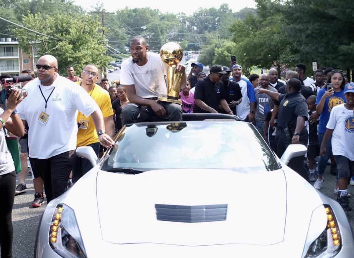 Kevin Durant sitting in a Chevrolet C7 Corvette holding the Larry O'Brien NBA Championship trophy