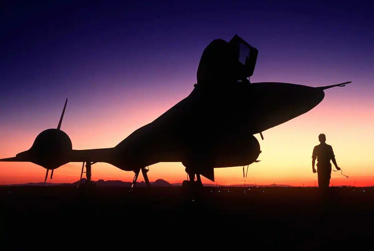 An SR-71 parked on the apron at an airbase, silhouetted by the sunset.