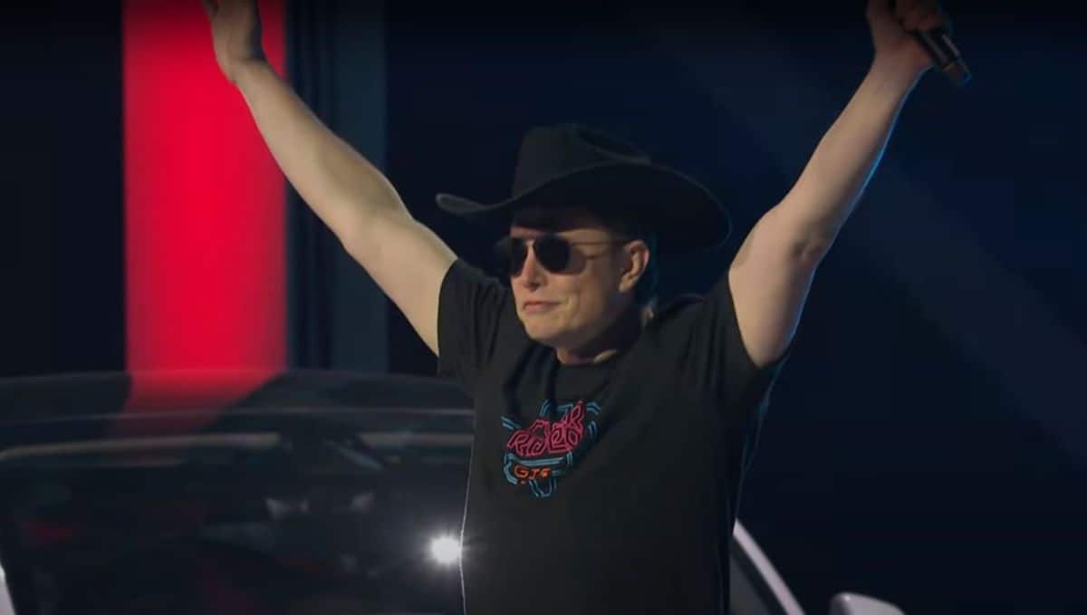 Elon Musk at Cyber Rodeo wearing a cowboy hat with his hands up in Texas.
