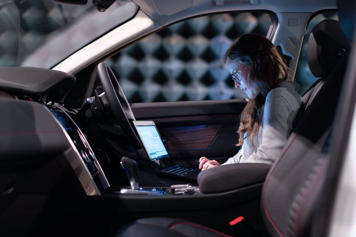 A woman uses a laptop on the front seat of her car.