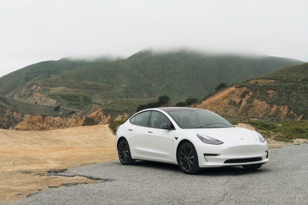 A Tesla Model 3 parked near a mountain.