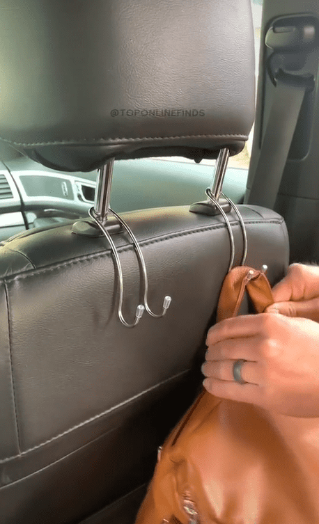 A person's hands using purse hooks attached to the back of the driver's seat.