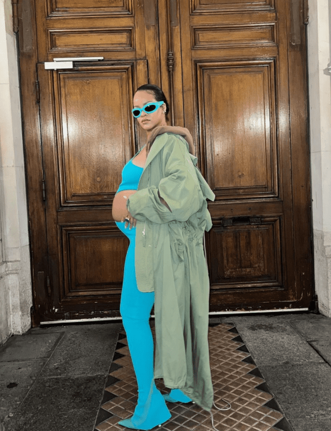 Rihanna shows off her baby bump while wearing a blue matching set and a coat draped over her.
