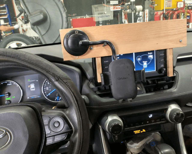 A photo shows a homemade phone mount made of wood attached to a car dashboard.